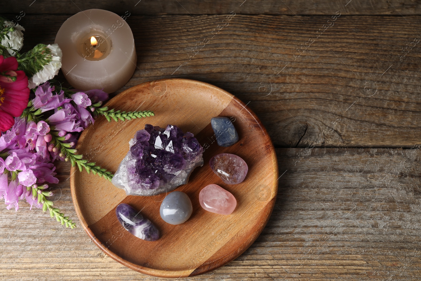 Photo of Different beautiful gemstones, flowers and burning candle on wooden table, flat lay. Space for text
