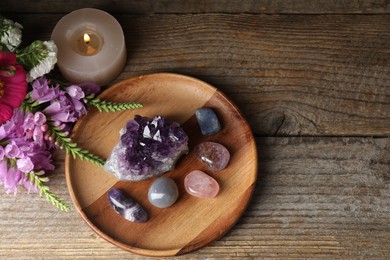Photo of Different beautiful gemstones, flowers and burning candle on wooden table, flat lay. Space for text