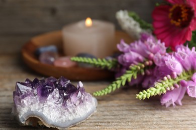 Photo of Different beautiful gemstones, flowers and burning candle on wooden table, closeup
