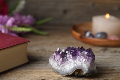 Photo of Beautiful amethyst gemstone, book, flowers and burning candle on wooden table, closeup