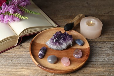 Photo of Different beautiful gemstones, book, flowers, palo santo and burning candle on wooden table, closeup
