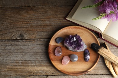 Photo of Different beautiful gemstones, book, flowers and palo santo on wooden table, flat lay. Space for text