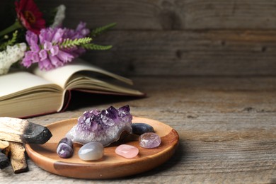 Photo of Different beautiful gemstones, book, flowers and palo santo on wooden table, closeup. Space for text