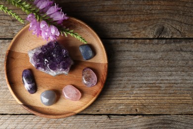 Photo of Different beautiful gemstones and flowers on wooden table, flat lay. Space for text