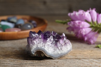 Photo of Different beautiful gemstones and flowers on wooden table, closeup