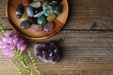 Photo of Different beautiful gemstones and flowers on wooden table, flat lay. Space for text