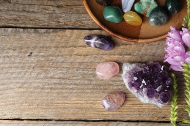 Photo of Different beautiful gemstones and flowers on wooden table, flat lay. Space for text