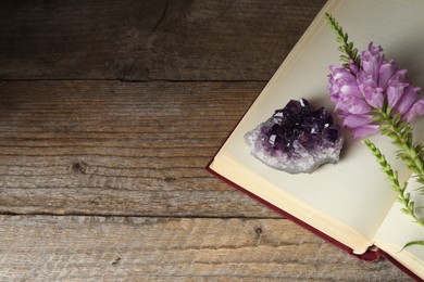 Photo of Beautiful amethyst gemstone, flowers and book on wooden table, above view. Space for text