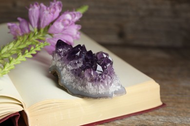 Photo of Beautiful amethyst gemstone, flowers and book on wooden table, closeup