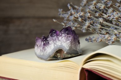 Photo of Beautiful amethyst gemstone, book and lavender flowers on blurred background, closeup