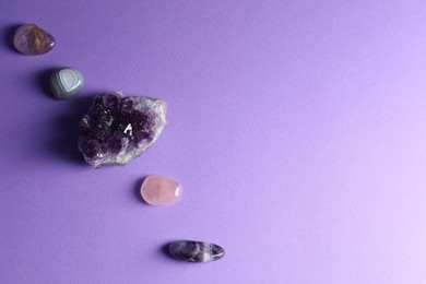 Photo of Different beautiful gemstones on purple background, flat lay. Space for text