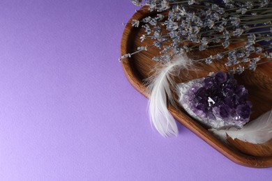 Photo of Beautiful amethyst gemstone, feathers and lavender flowers on purple background, above view. Space for text