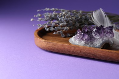 Photo of Beautiful amethyst gemstone, feather and lavender flowers on purple background, closeup. Space for text