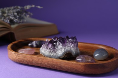 Photo of Beautiful amethyst gemstone, book and lavender flowers on purple background, closeup