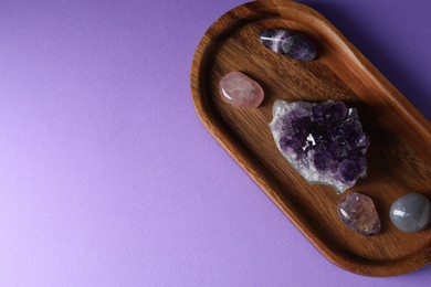 Photo of Different beautiful gemstones on purple background, top view. Space for text