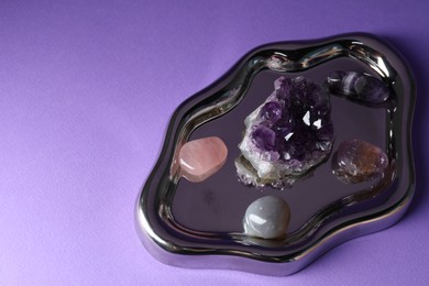 Photo of Different beautiful gemstones on purple background, closeup. Space for text