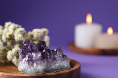 Photo of Beautiful amethyst gemstone, flowers and burning candles on purple background, closeup. Space for text