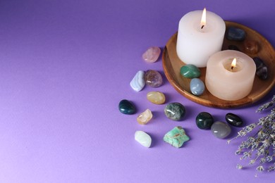 Photo of Different beautiful gemstones, lavender flowers and burning candles on purple background, above view. Space for text