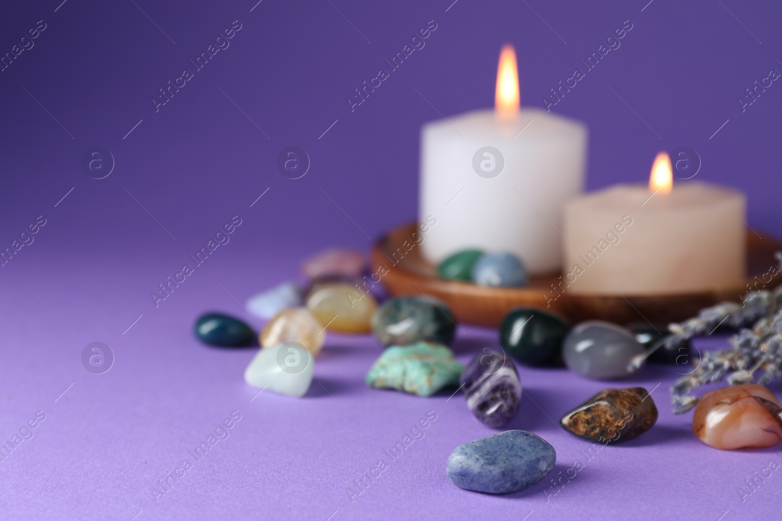 Photo of Different beautiful gemstones, lavender flowers and burning candles on purple background, closeup. Space for text