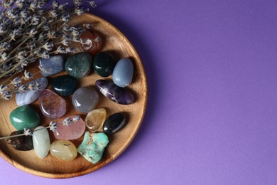 Photo of Different beautiful gemstones and lavender flowers on purple background, top view. Space for text