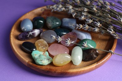 Photo of Different beautiful gemstones and lavender flowers on purple background, closeup