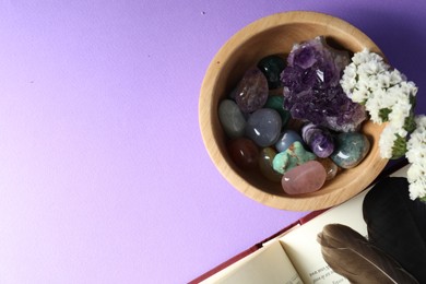 Photo of Different beautiful gemstones, feathers, flowers and book on purple background, flat lay. Space for text