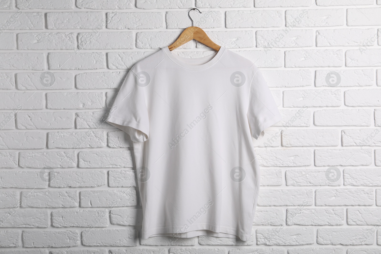 Photo of Hanger with t-shirt against white brick wall. Mockup for design