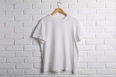 Photo of Hanger with t-shirt against white brick wall. Mockup for design