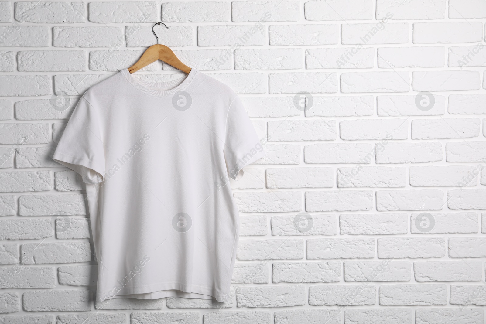 Photo of Hanger with t-shirt against white brick wall. Mockup for design