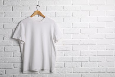 Photo of Hanger with t-shirt against white brick wall. Mockup for design