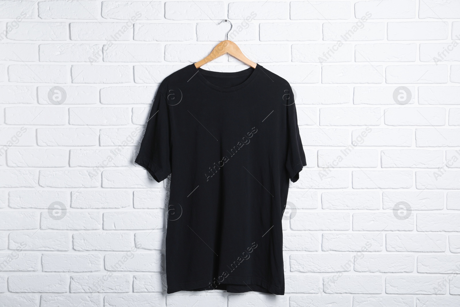Photo of Hanger with black t-shirt against white brick wall. Mockup for design