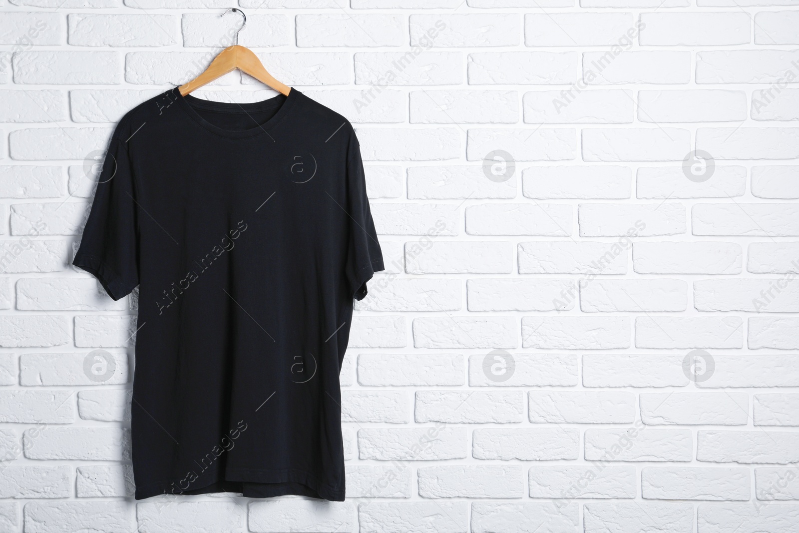 Photo of Hanger with black t-shirt against white brick wall. Mockup for design