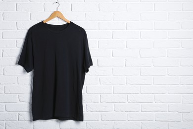 Photo of Hanger with black t-shirt against white brick wall. Mockup for design