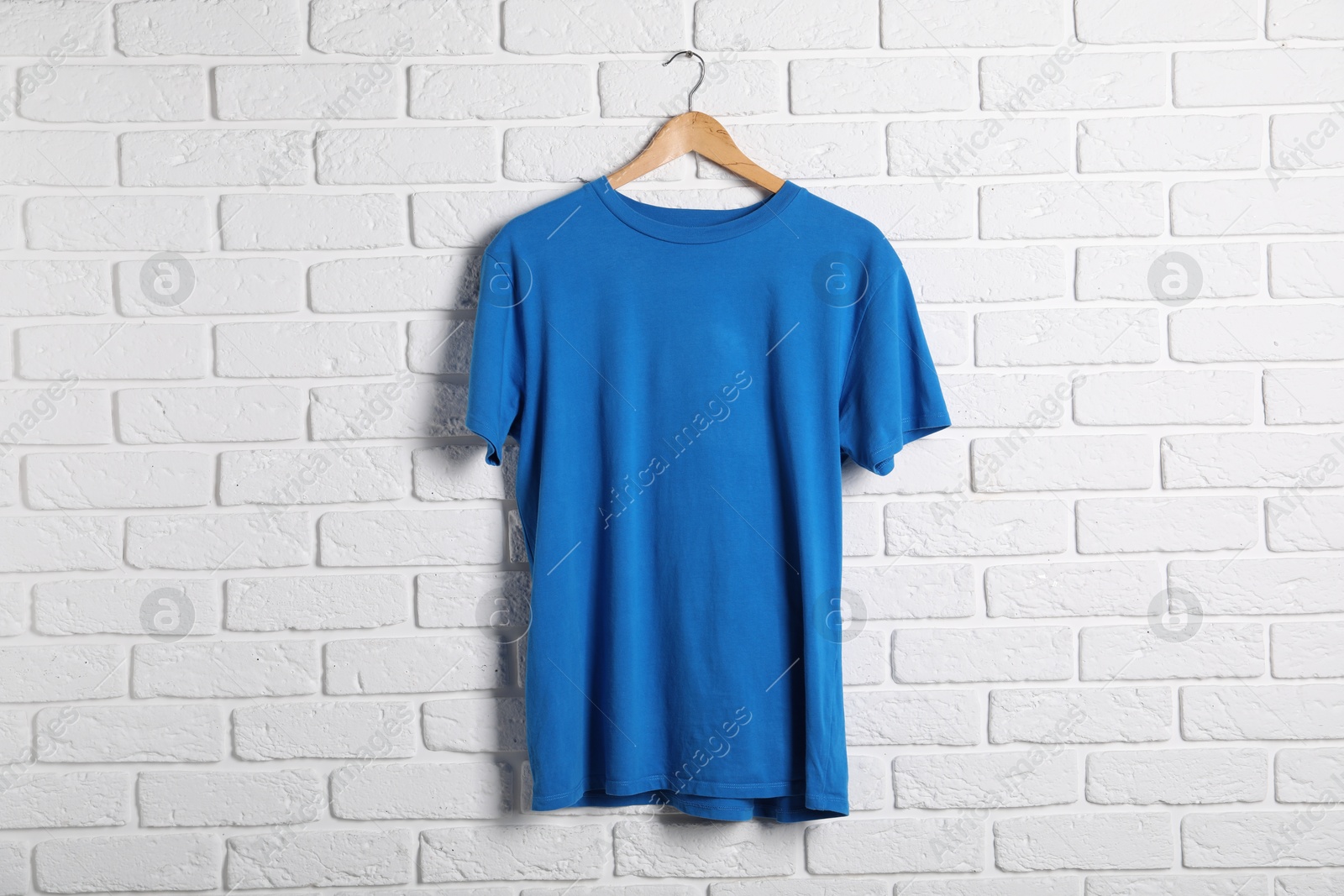 Photo of Hanger with blue t-shirt against white brick wall. Mockup for design