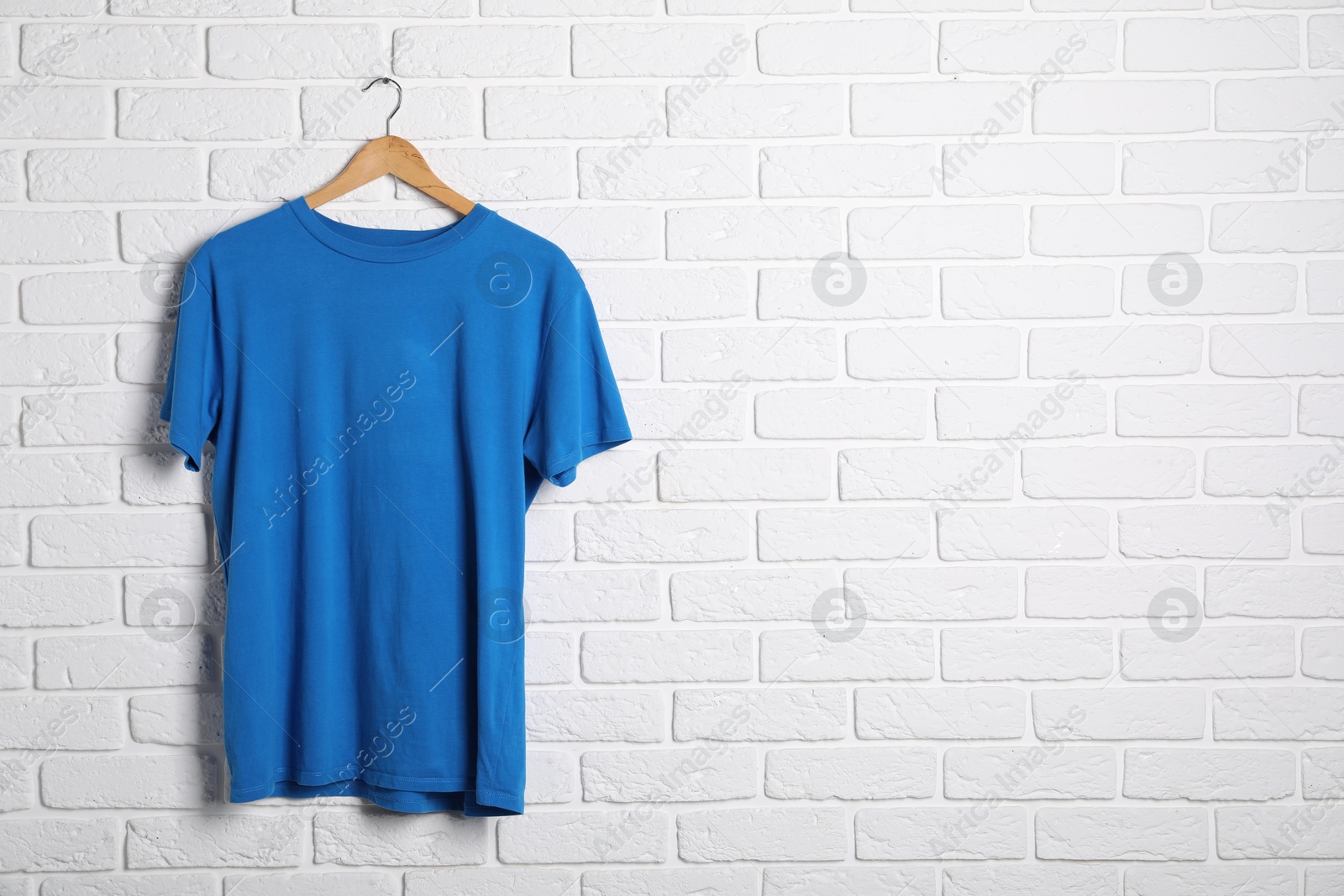 Photo of Hanger with blue t-shirt against white brick wall. Mockup for design