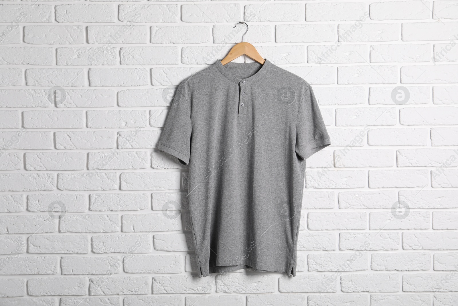 Photo of Hanger with grey t-shirt against white brick wall. Mockup for design