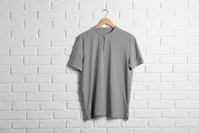 Photo of Hanger with grey t-shirt against white brick wall. Mockup for design