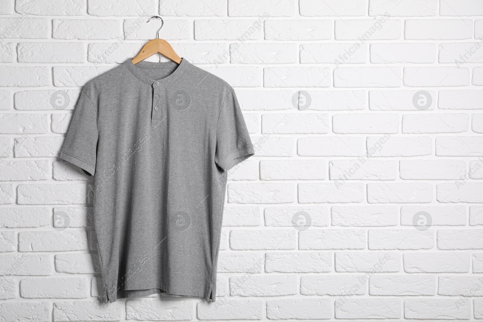 Photo of Hanger with grey t-shirt against white brick wall. Mockup for design