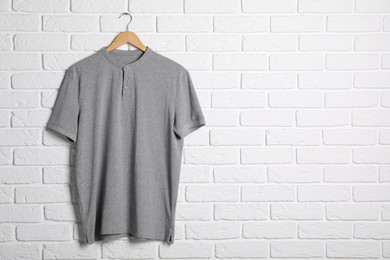 Photo of Hanger with grey t-shirt against white brick wall. Mockup for design