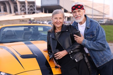 Photo of Stylish senior couple with takeaway coffee near modern cabriolet outdoors