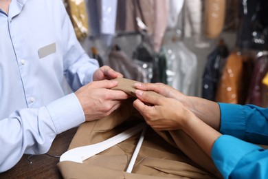 Photo of Dry-cleaning service. Worker receiving jacket from client at counter indoors, closeup