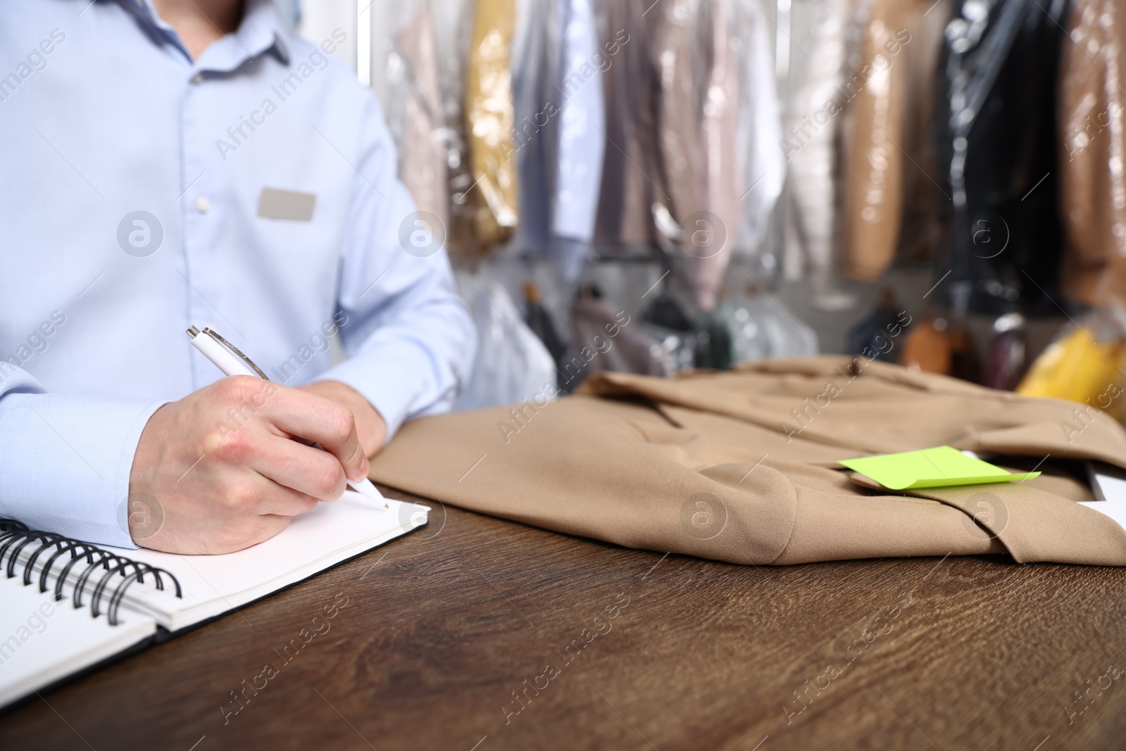 Dry-cleaning service. Worker with jacket writing in notebook at counter indoors, closeup Photo of Dry-cleaning service. Worker with jacket writing in notebook at counter indoors, closeup