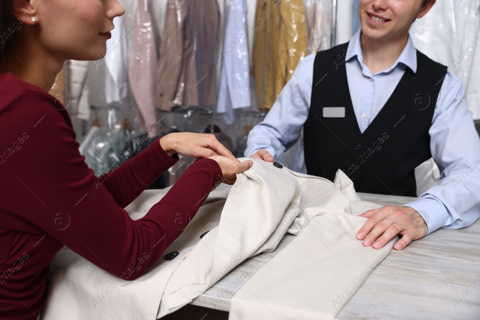 Photo of Dry-cleaning service. Worker receiving jacket from client at counter indoors, closeup