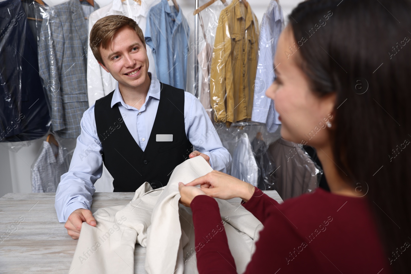 Photo of Dry-cleaning service. Happy worker receiving jacket from client at counter indoors