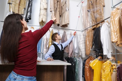 Photo of Dry-cleaning service. Happy worker choosing clothes from rack for client indoors, low angle view