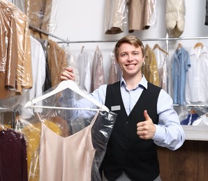 Photo of Dry-cleaning service. Happy worker holding dress in plastic bag indoors
