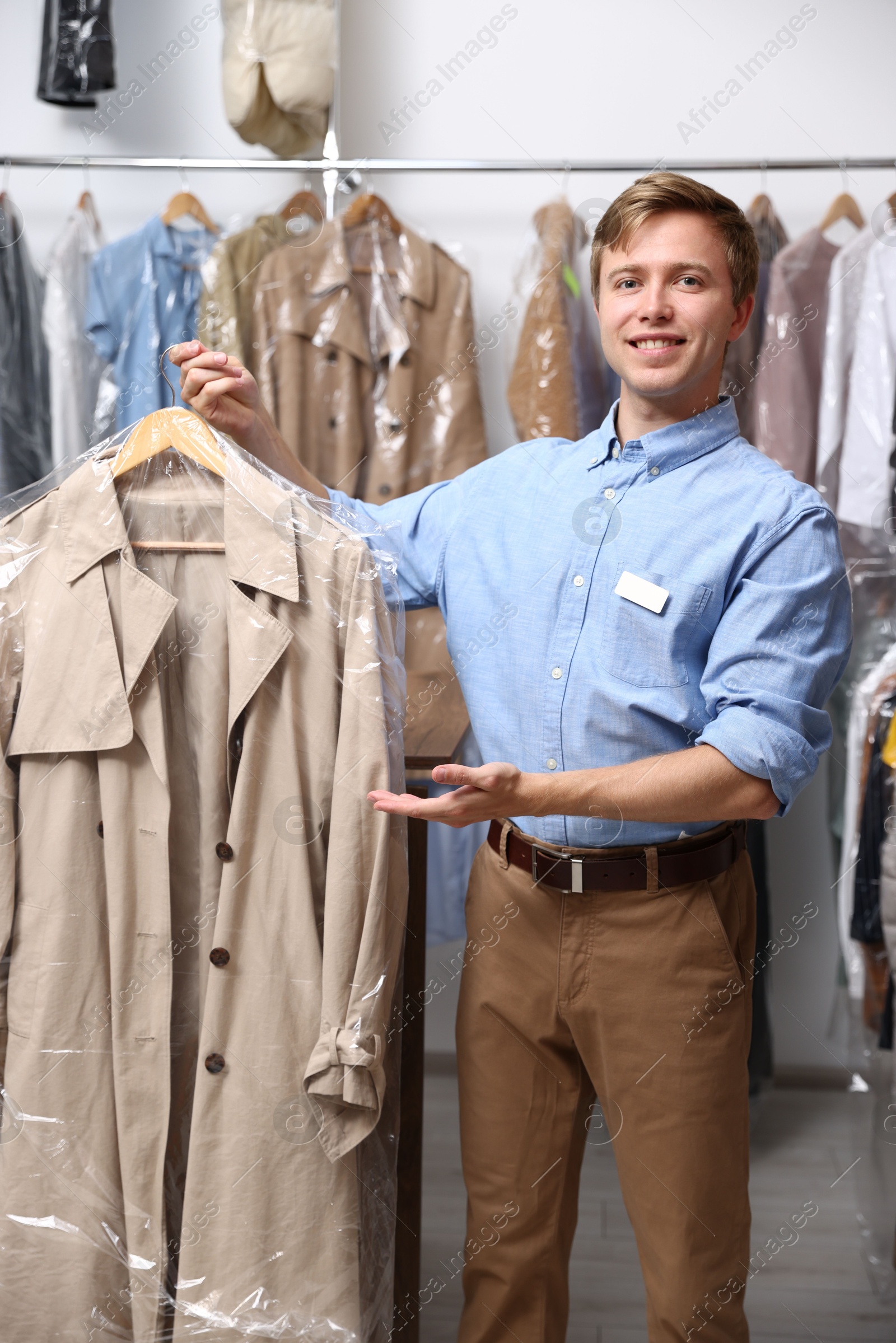 Photo of Dry-cleaning service. Happy worker holding coat in plastic bag indoors