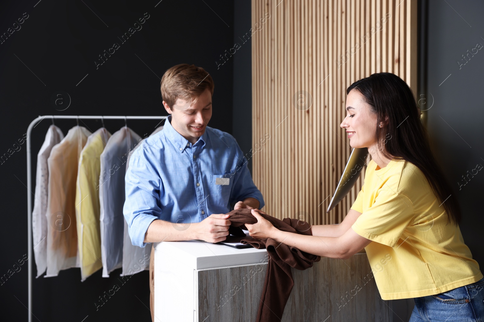Photo of Dry-cleaning service. Happy worker receiving sweater from client at counter indoors