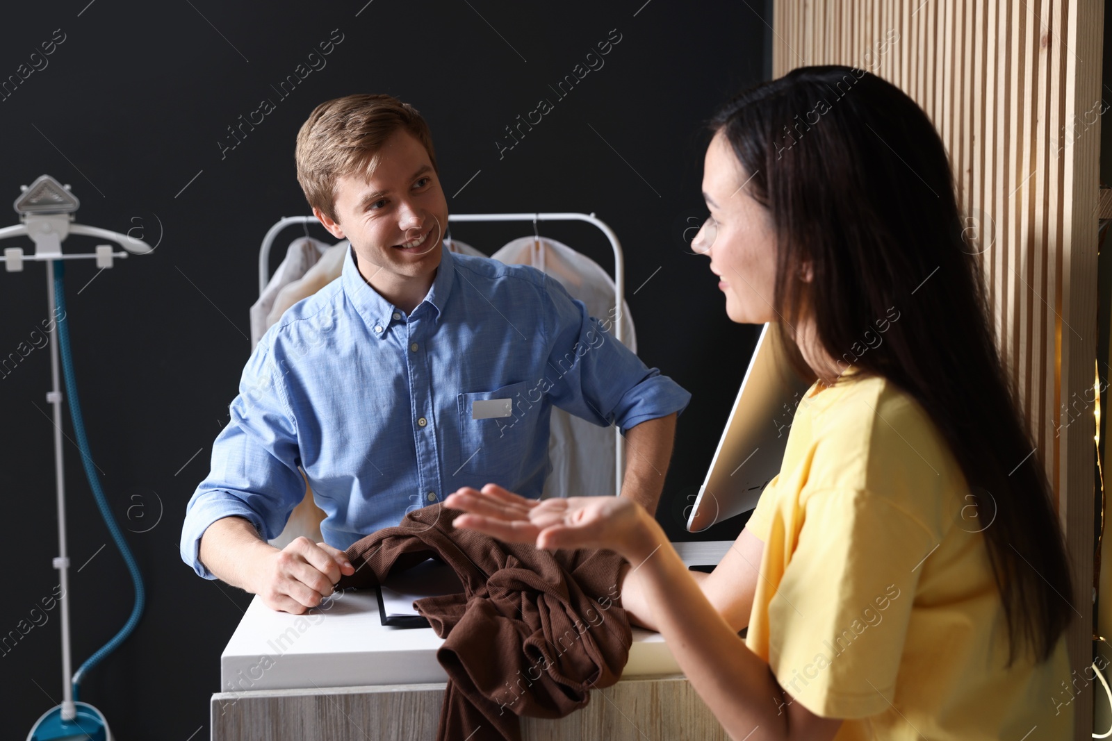 Photo of Dry-cleaning service. Happy worker receiving sweater from client at counter indoors
