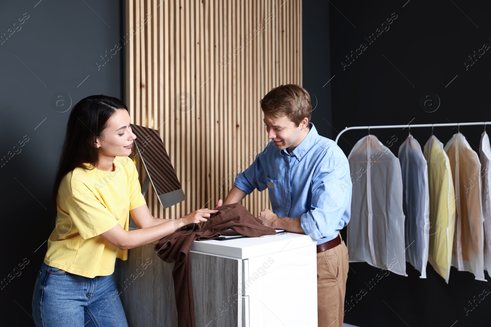 Photo of Dry-cleaning service. Happy worker receiving sweater from client at counter indoors